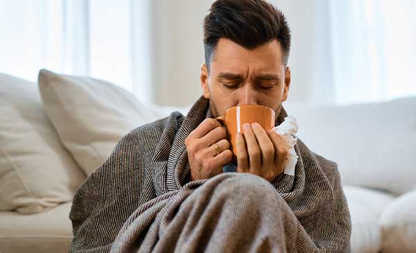 man curled up in blanket sipping the best tea for a cold