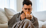man curled up in blanket sipping the best tea for a cold