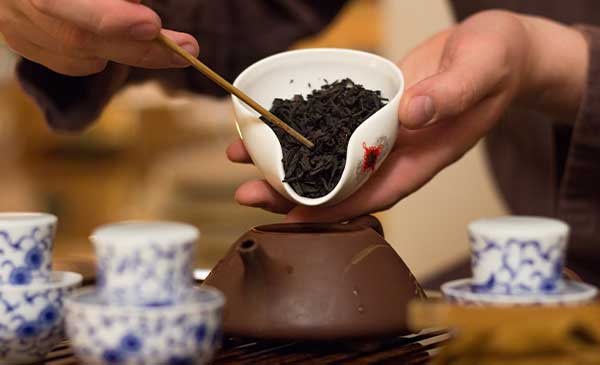 tea master scooping black tea into teapot