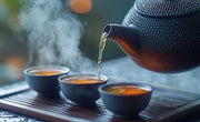 black tea pot pouring oolong tea into small cups with steam rising