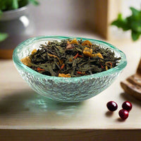 Cranberry apple green tea in a textured glass bowl on a wooden surface with cranberries alongside