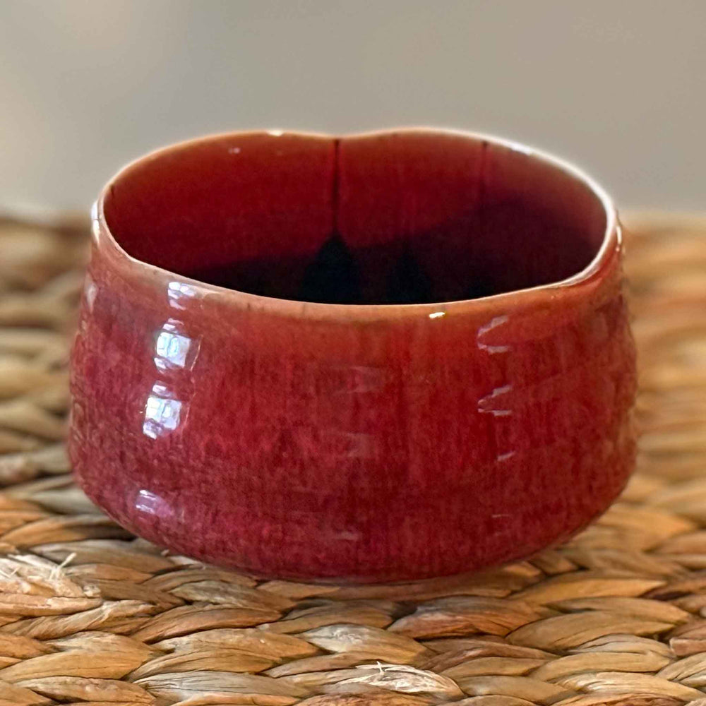 Red handmade ceramic matcha bowl on a woven surface