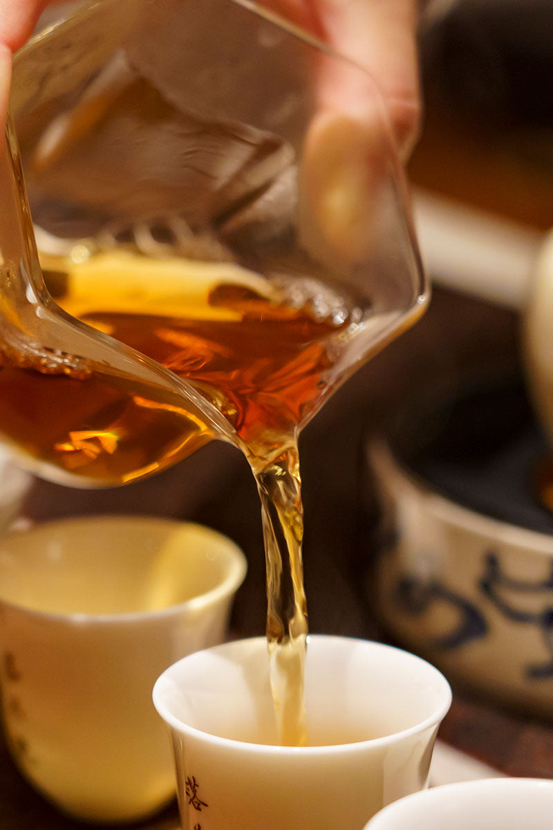 Formosa Oolong tea being poured from a glass teapot into a white cup with a blurred background