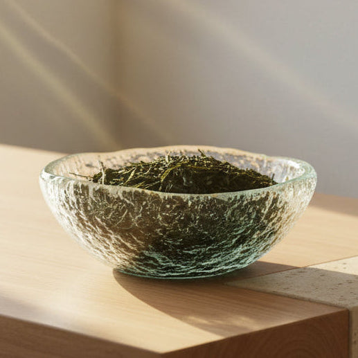 Clear glass bowl filled with japanese sencha green tea leaves on a wooden counter