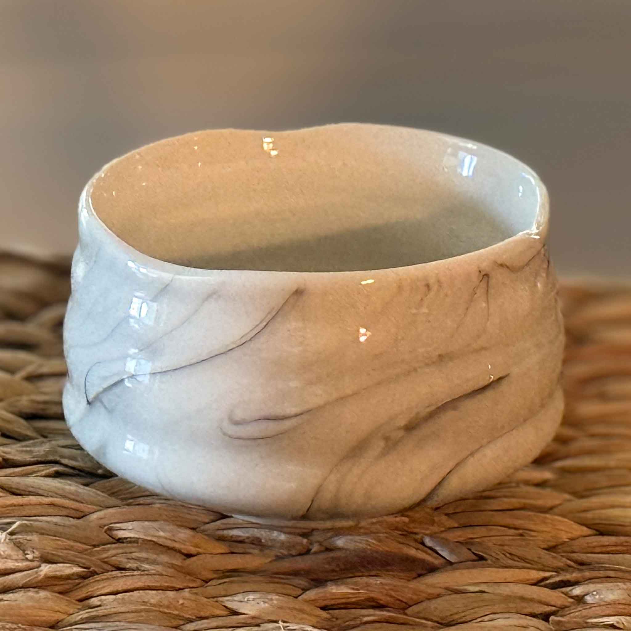 handmade ceramic matcha bowl with marbled design on a woven surface