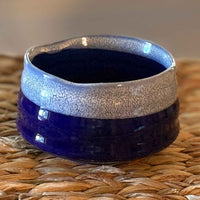 handmade ceramic matcha bowl with blue and white glaze on a woven surface