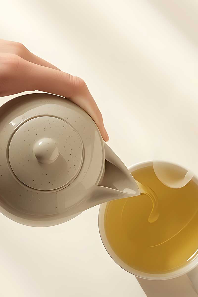Hand pouring green tea for weightloss from a teapot into a cup on a soft beige background