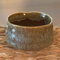 handmade ceramic matcha bowl with a textured surface on a woven mat