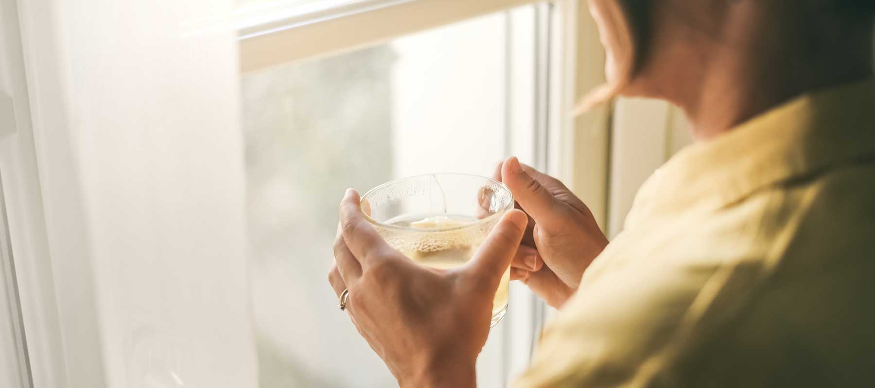 Person holding a cup of tea by a window with soft light during a winter reset