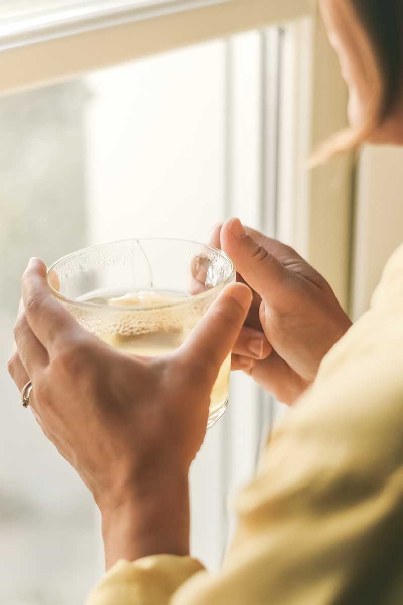 Person holding a cup of tea by a window with soft light during a winter reset